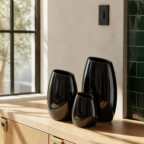 Set of three glossy black ceramic vases on white oak joinery in a sunlit modern room