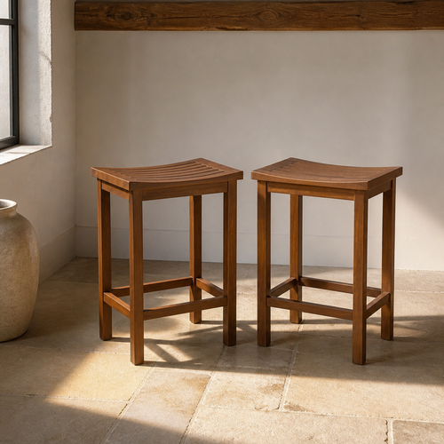Set of two acacia wood counter height bar stools with saddle scooped slatted seats on a limestone flag floor