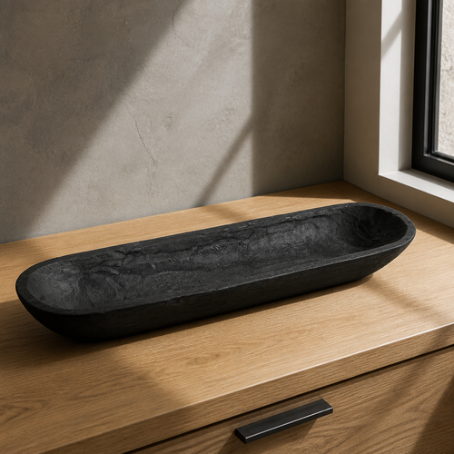 Long black hand-carved wooden dough bowl on a light oak counter against a microcement wall