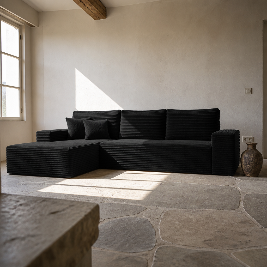 Low angle of the black corduroy chaise sectional and its bolster pillows in a hard sun patch