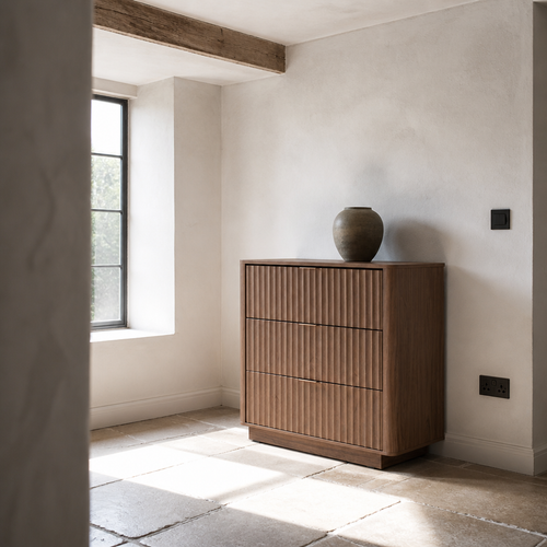 Fluted walnut dresser on a limestone flag floor beneath an exposed timber beam