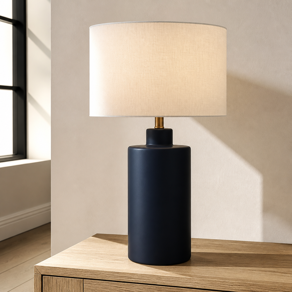 Carlina matte navy ceramic table lamp with white linen drum shade on pale oak in a warm white plaster room