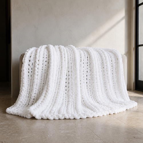 White chunky chenille knit throw blanket, 80 by 90 inches, draped over a bench against a bone plaster wall