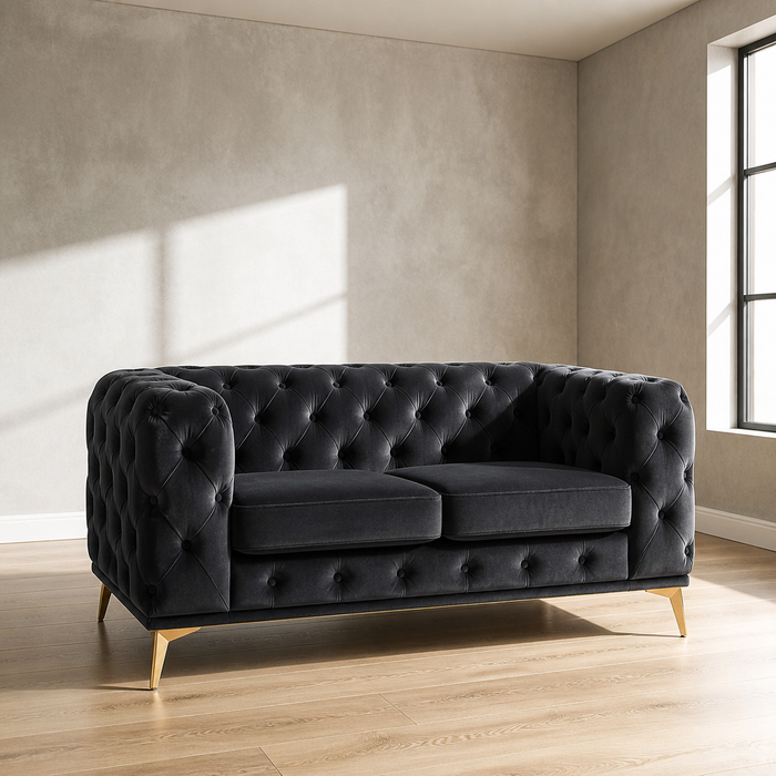 Black velvet Chesterfield loveseat with deep diamond button tufting and brass legs, 61.25 inches wide, against a microcement wall