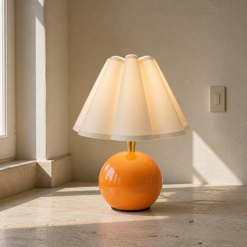 Orange ceramic ball table lamp with a pleated ivory petal shade on travertine