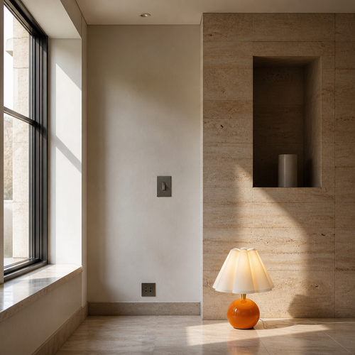 Small orange ceramic lamp in a travertine gallery room with a deep window reveal