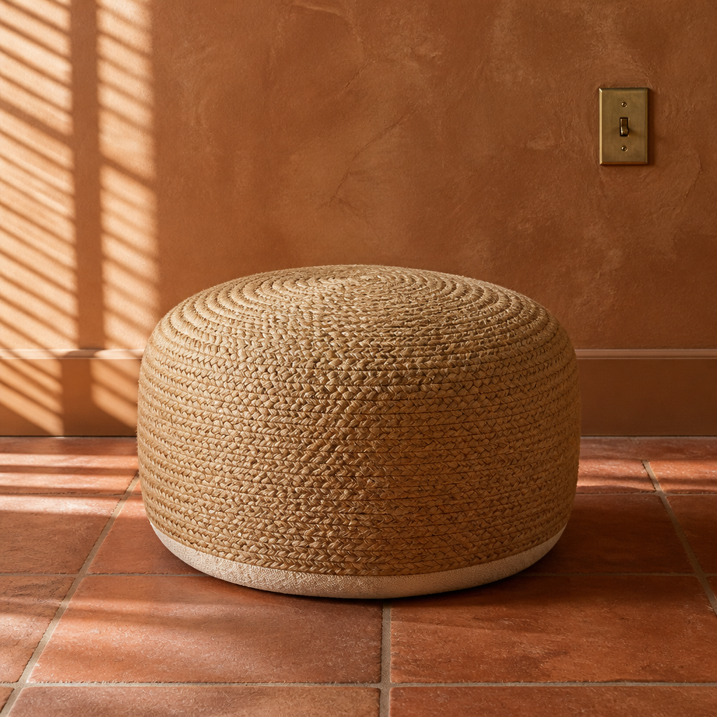 Circular braided jute ottoman pouf, 18 inches across and 10 inches tall, on a terracotta tile floor against a rust clay plaster wall