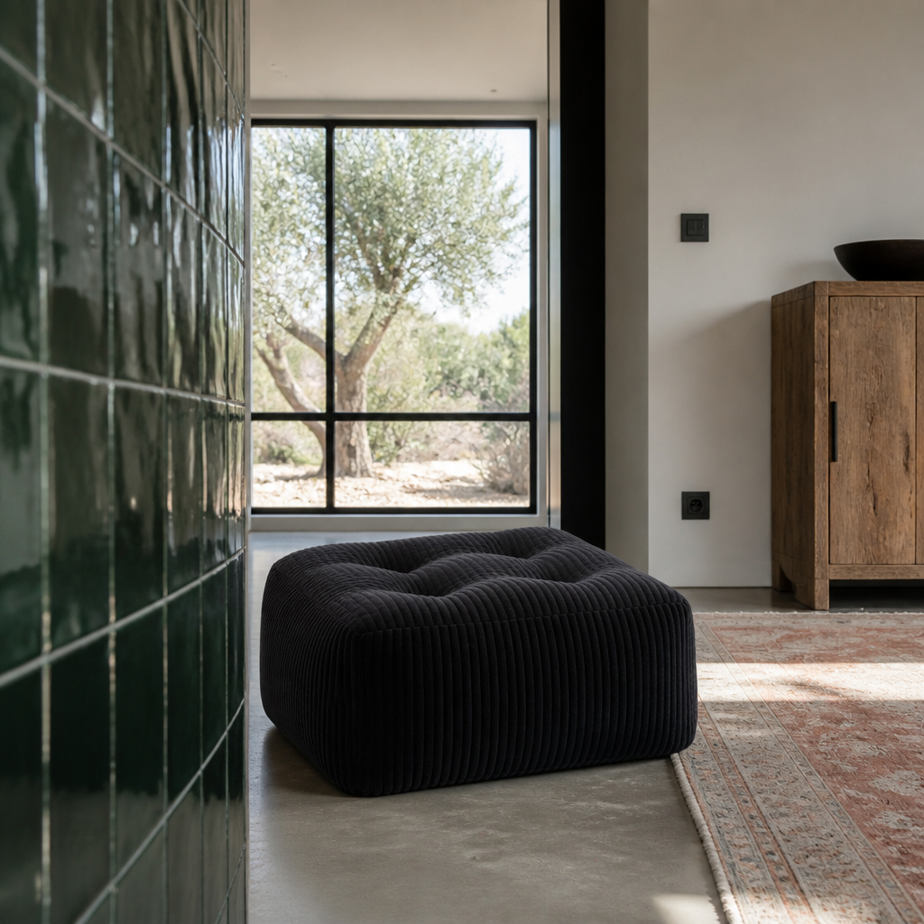 Square black corduroy pouf low against a deep green zellige tile panel