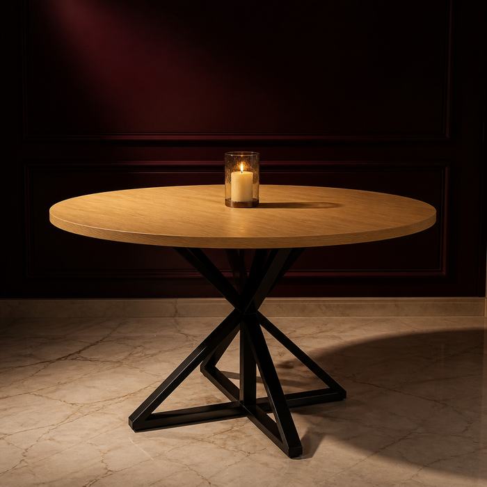 Farmhouse Metal Dining Table with a round wood effect top on a sculptural black steel intersecting base, styled in a warm evening dining room
