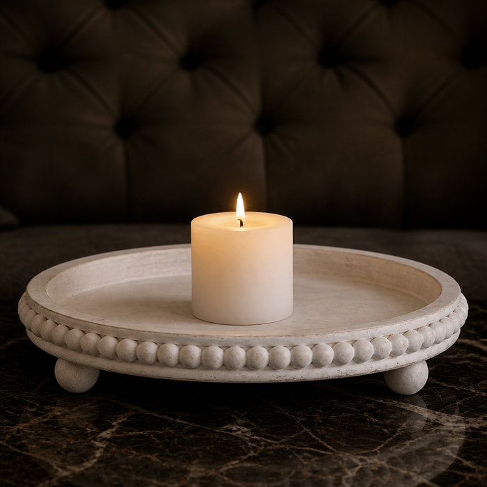 Round whitewashed wood tray with a beaded rim and three ball feet, holding a lit candle